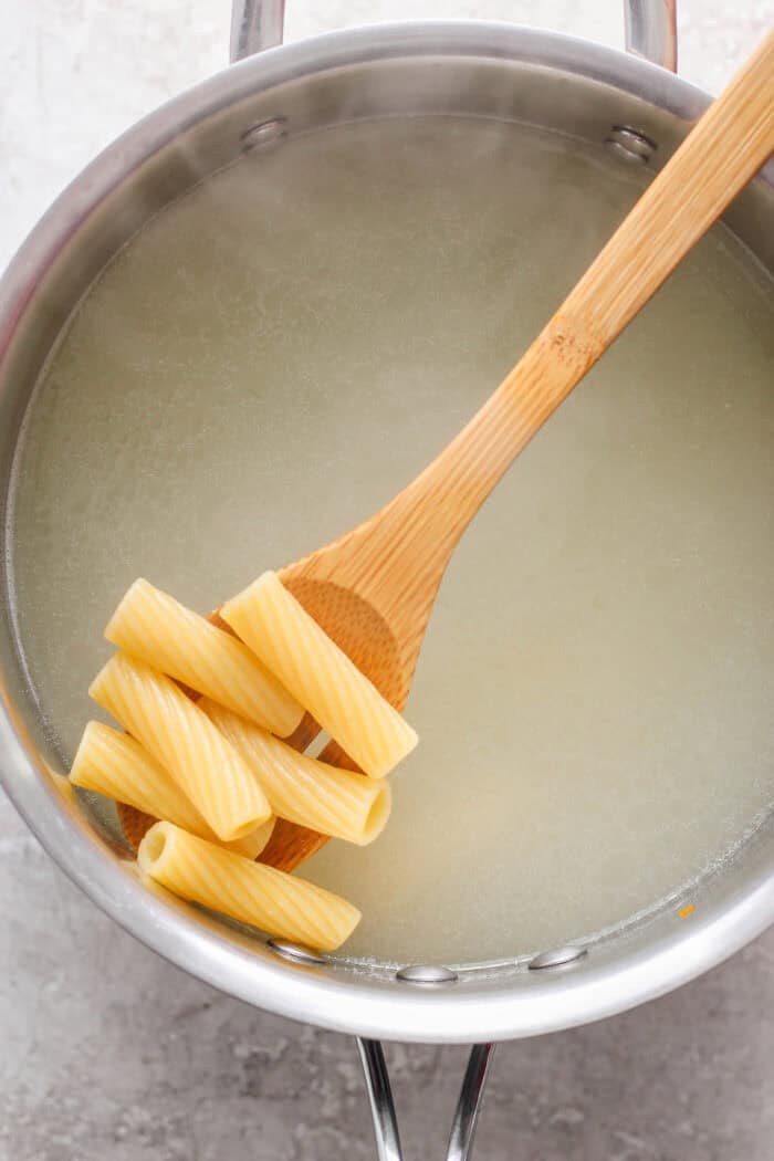 A wooden spoon scoops out pasta from a pot of water.