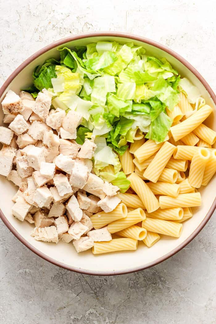 All of the ingredients for Caesar chicken pasta salad minus the dressing are placed in a big bowl.