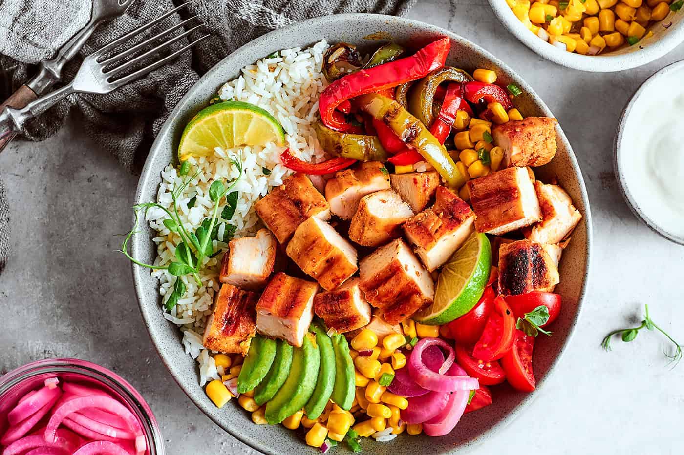 overhead photo of a fajita bowl with rice, chicken, corn salsa, pickled red onions, peppers, and avocado