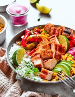 a fajita bowl with rice, chicken, corn salsa, pickled red onions, peppers, and avocado