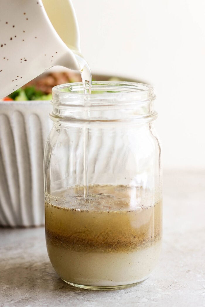 Dressing ingredients are poured into a glass jar.