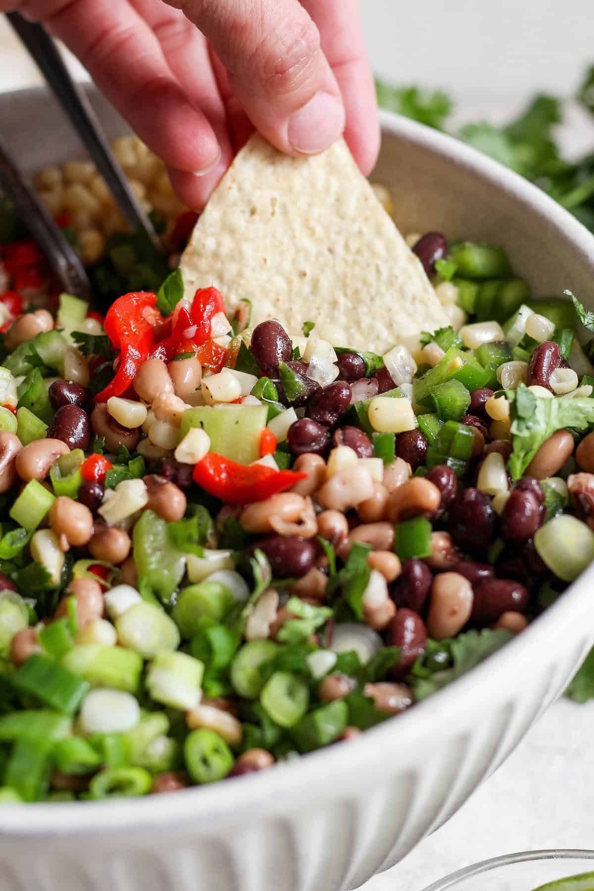 A hand dips a corn chip into a bowl of cowboy caviar.