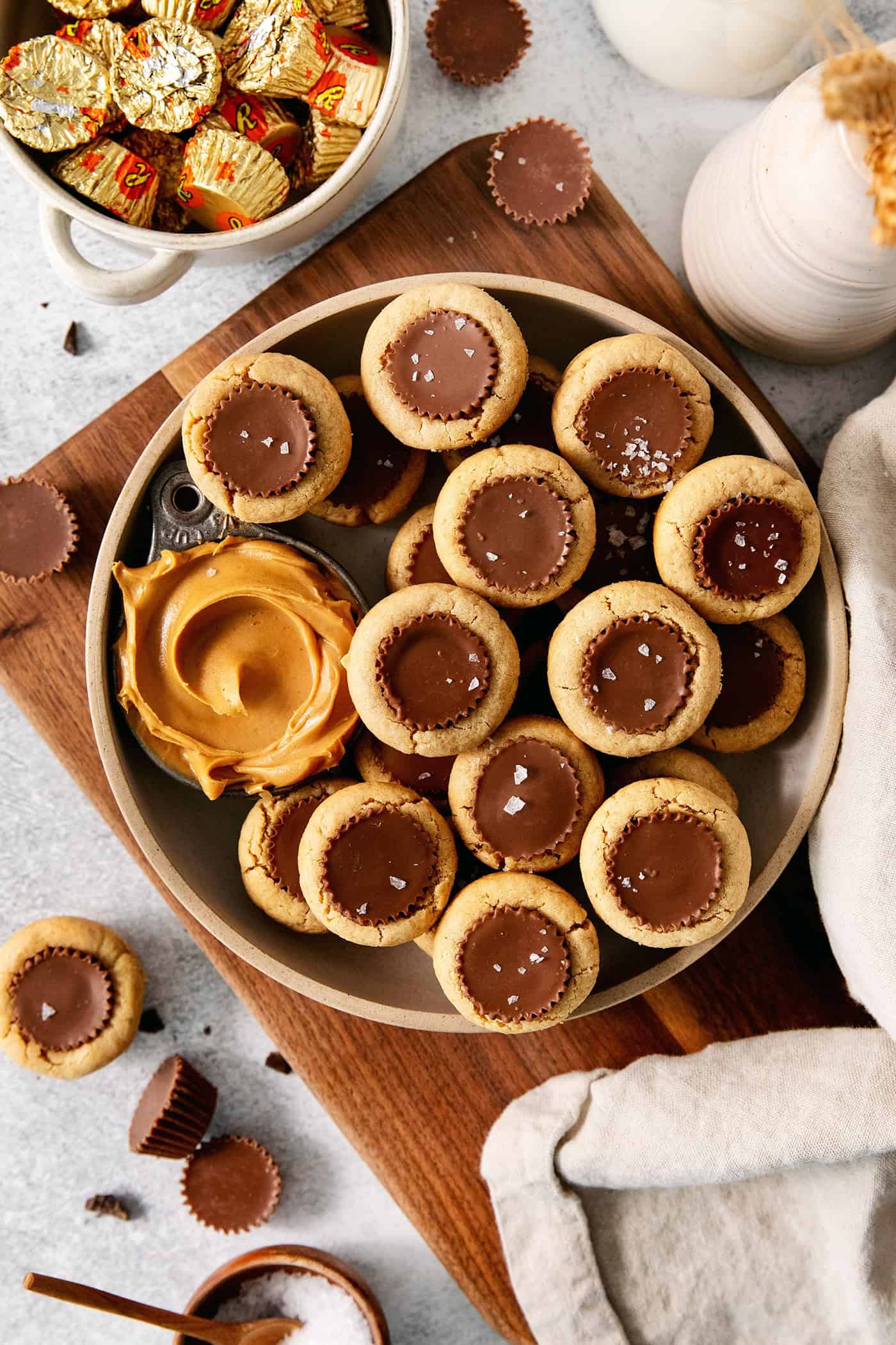 A big bowl of peanut butter cup cookies along with a small bowl of peanut butter plus a bowl of mini peanut butter cups.