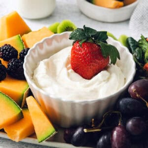 A strawberry is dipped into a bowl of fruit dip.