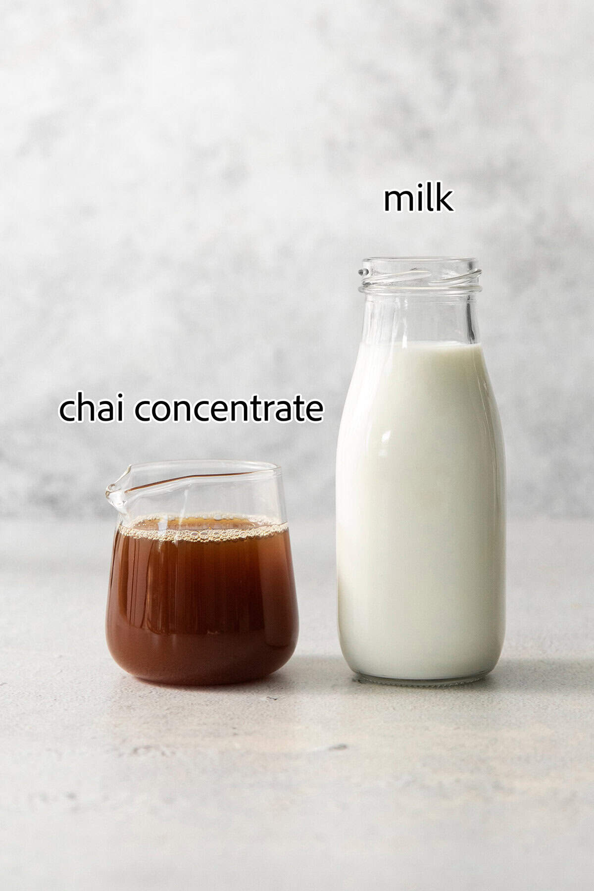 Ingredients needed for a chai latte are shown labeled in glass containers: chai concentrate, milk.