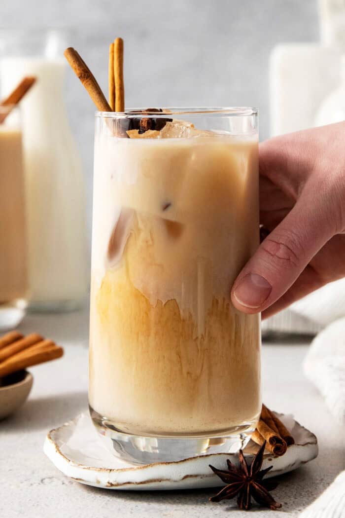 A hand reaches for a glass of iced chai latte.