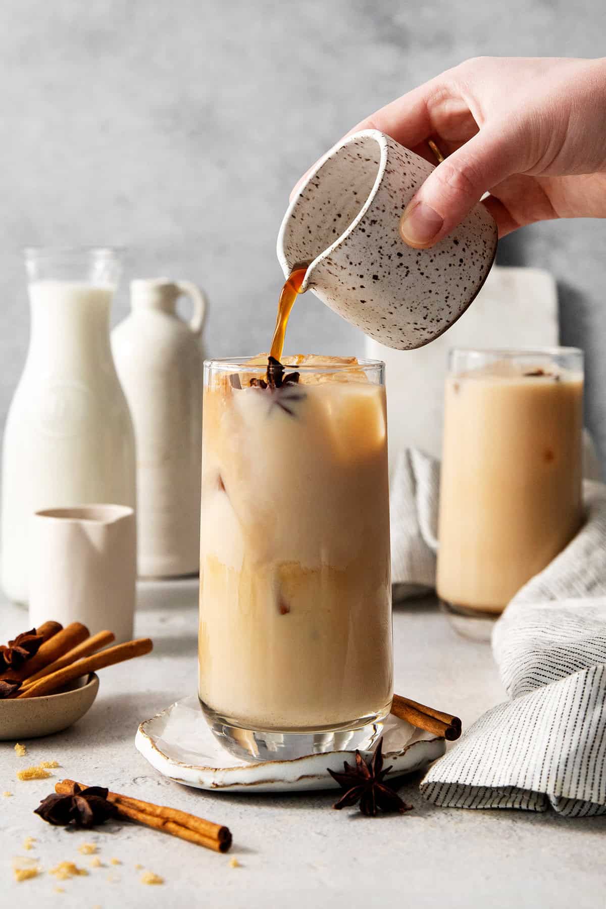 A hand pours espresso into an iced chai latte.