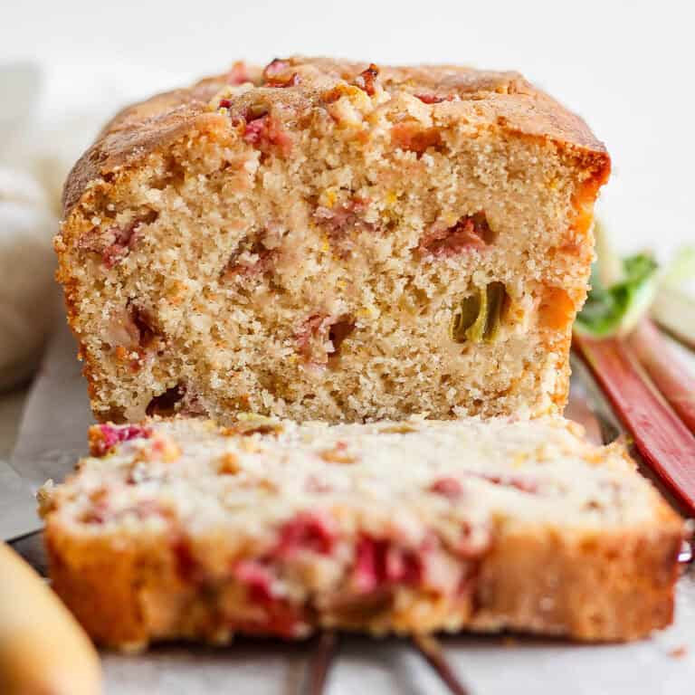 A loaf of rhubarb bread cut to show a slice and the pink spots of rhubarb.