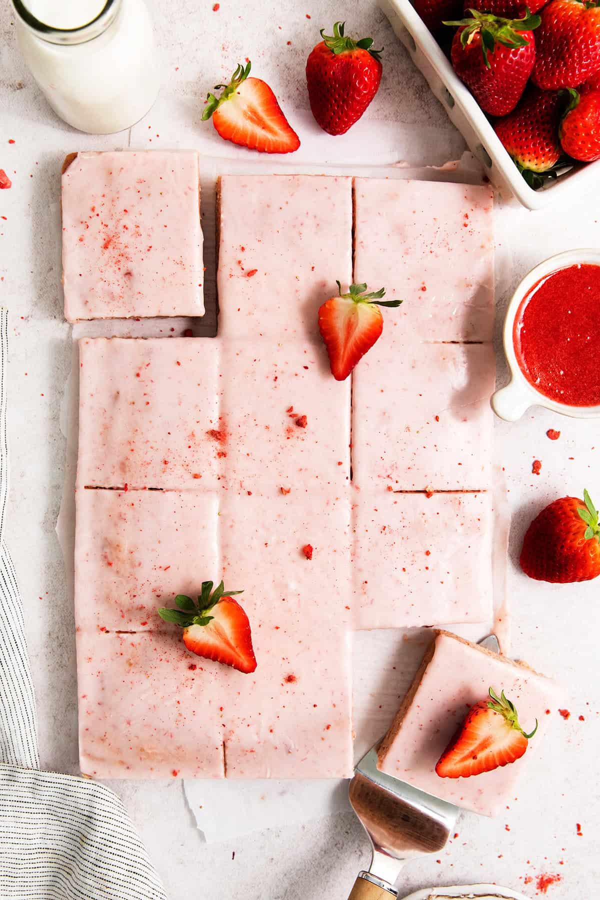 These homemade Strawberry Brownies feature pretty, strawberry-infused bars topped with thick strawberry icing for even more berry flavor. Pink icing-topped strawberry brownies are cut into squares, with strawberries scattered around them.