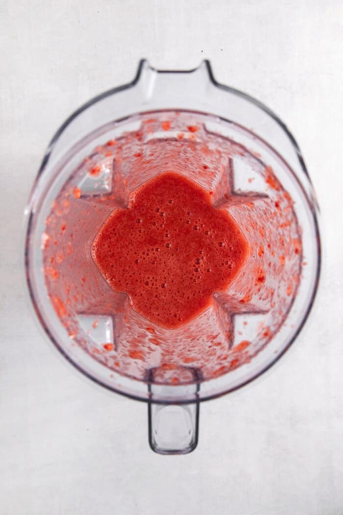 Strawberries and sugar are pureed until smooth in a blender.
