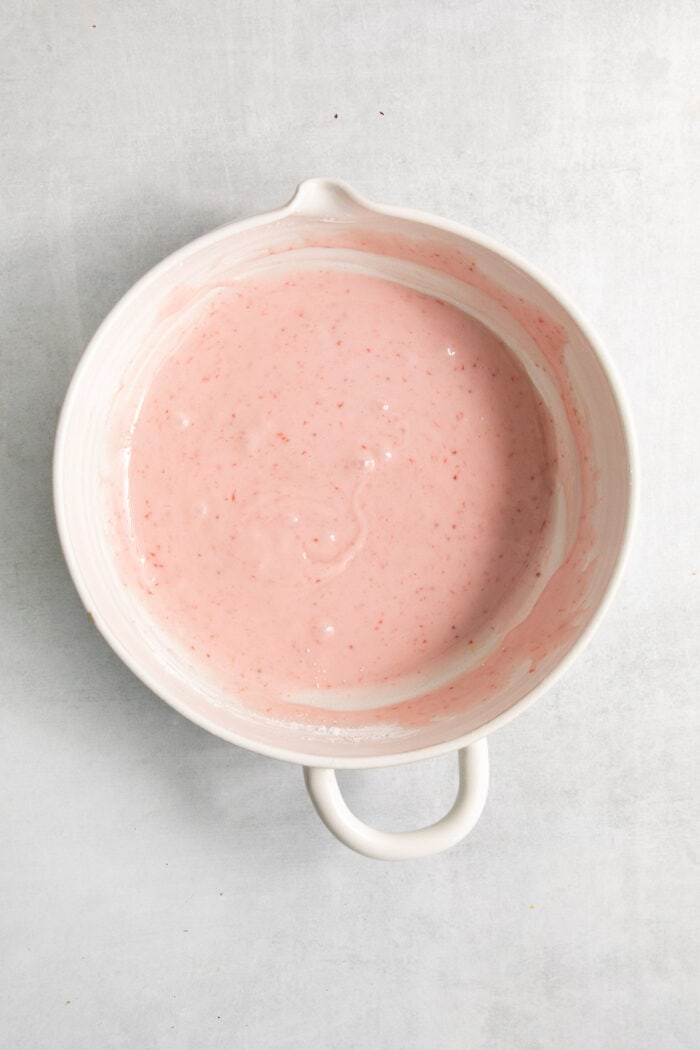 Strawberry icing is mixed in a bowl.