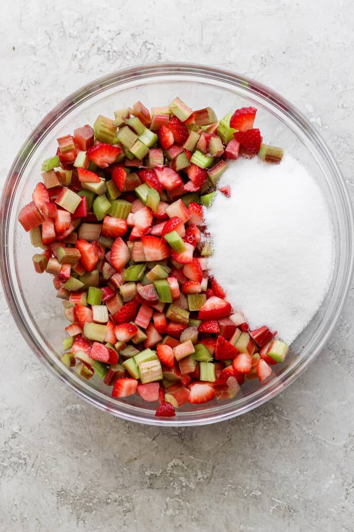 chopped strawberries and rhubarb in a clear mixing bowl with sugar