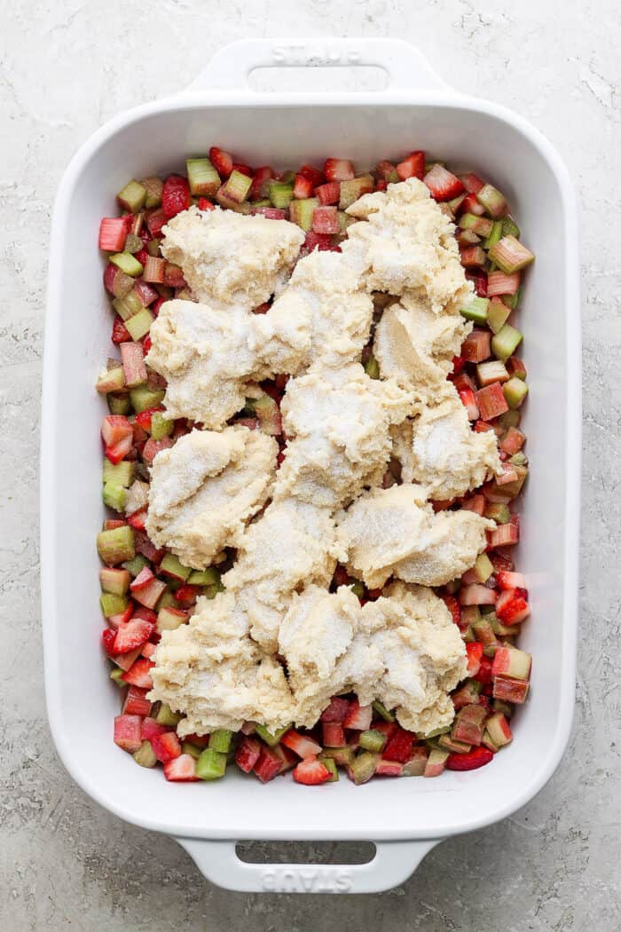strawberry rhubarb filling in a white rectangle baking dish, with dollops of cobbler dough over the top, ready to go in the oven