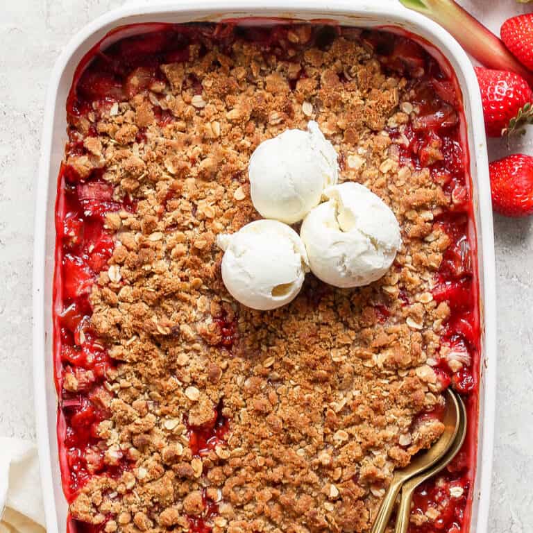 strawberry rhubarb crisp in a white rectangular baking dish, with scoops of ice cream on top