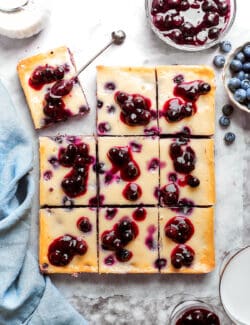 Nine pieces of blueberry cheesecake bars are shown cut into pieces.