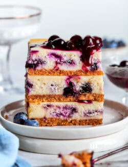 a stack of 3 blueberry cheesecake bars on a white plate