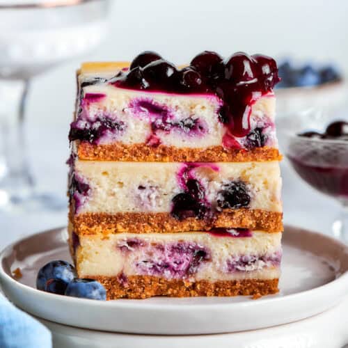 a stack of 3 blueberry cheesecake bars on a white plate