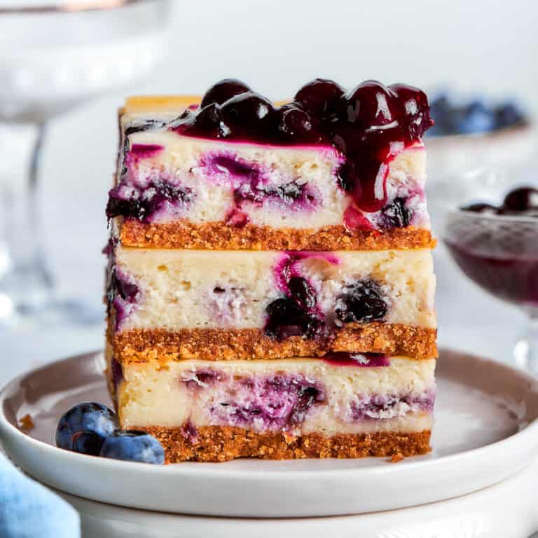 a stack of 3 blueberry cheesecake bars on a white plate