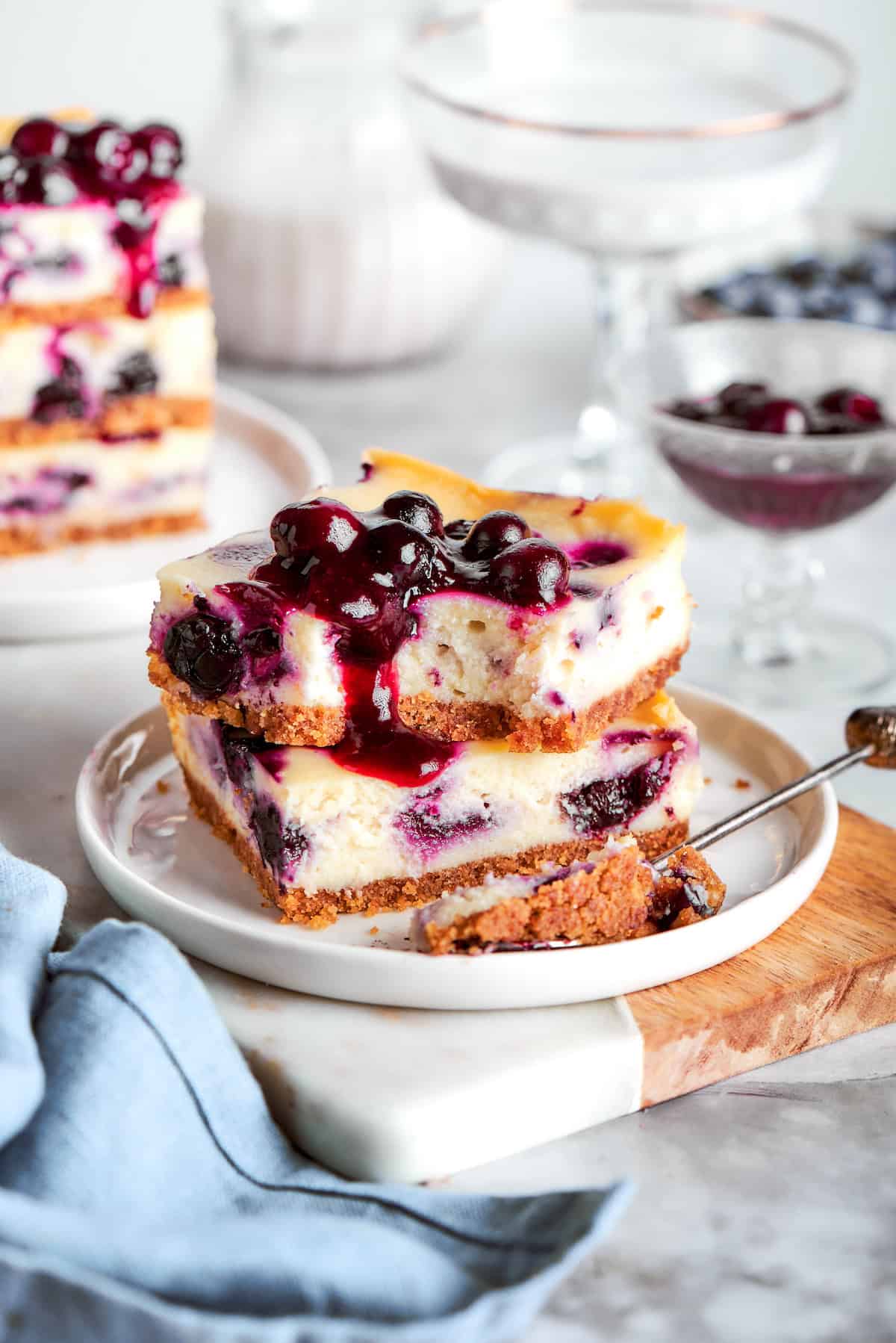 A plate on a table with two blueberry cheesecake bars stacked on top of each other.