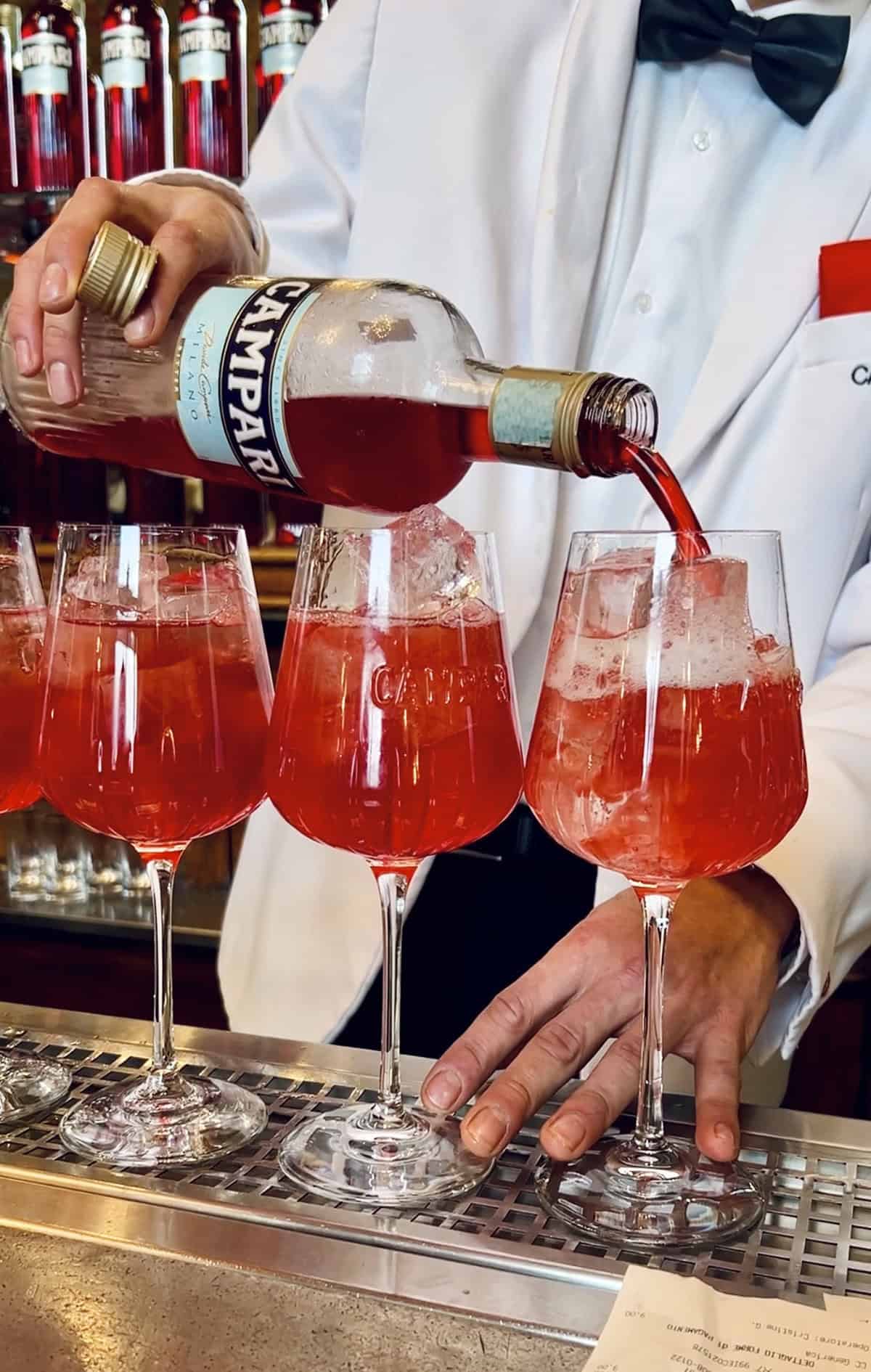 a bartender at Camparino in Milan, pouring Campari into glasses, creating Campari Spritz cocktails