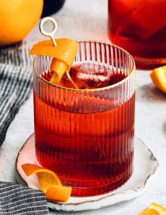A Negroni is served with orange peel on a white plate.
