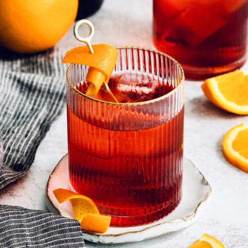 A Negroni is served with orange peel on a white plate.