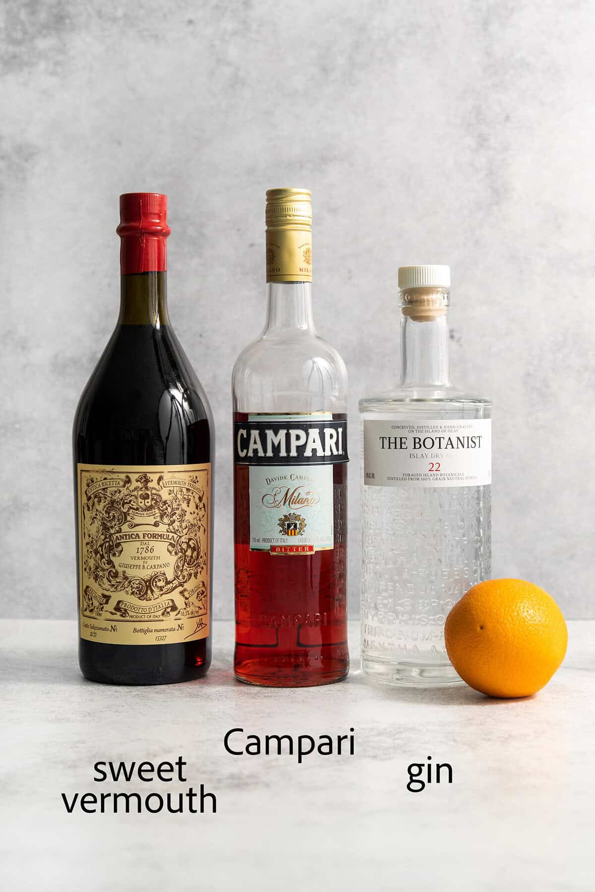 This classic Italian Negroni recipe features an easy 1-1-1 ratio of gin, Campari, and sweet vermouth and is served over ice. Ingredients for Negroni are shown: gin, campari, sweet vermouth, and orange.