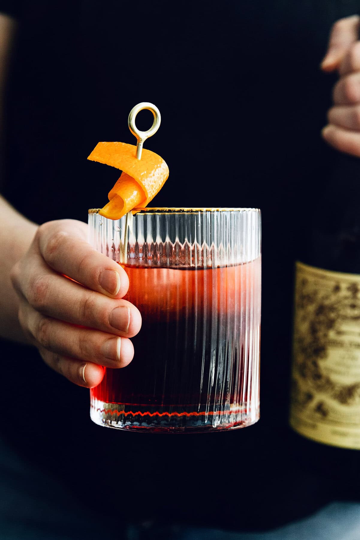 A hand presents a Negroni topped with a twist of orange.