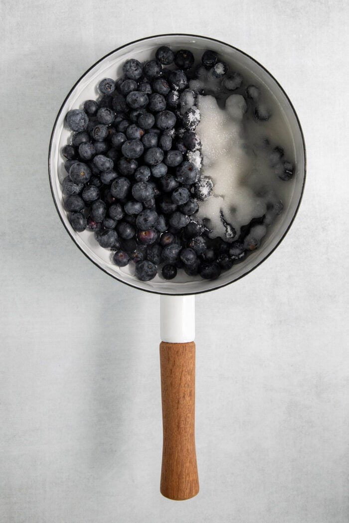 Blueberries are combined with other ingredients in a pot for blueberry sauce.