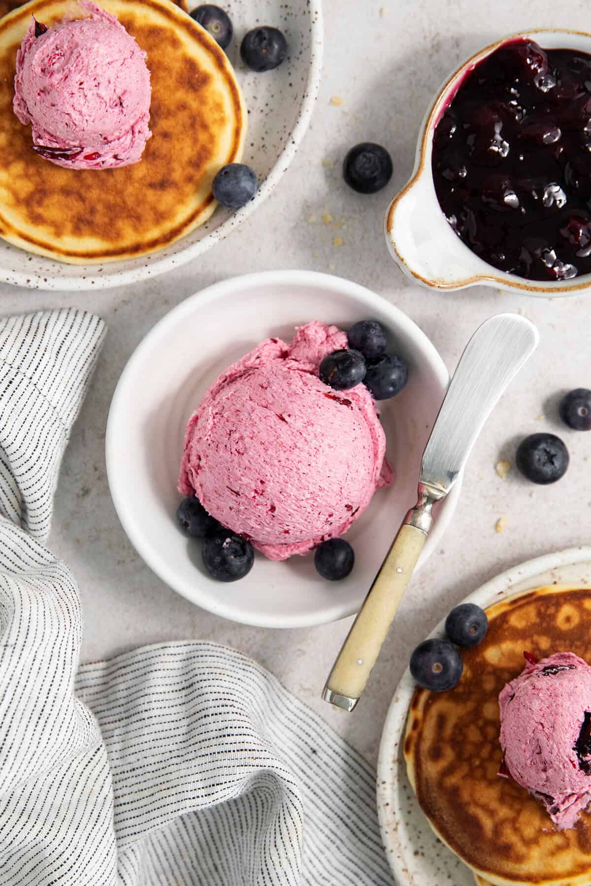 Pancakes on plates topped with blueberry butter and a bowl of blueberry butter.