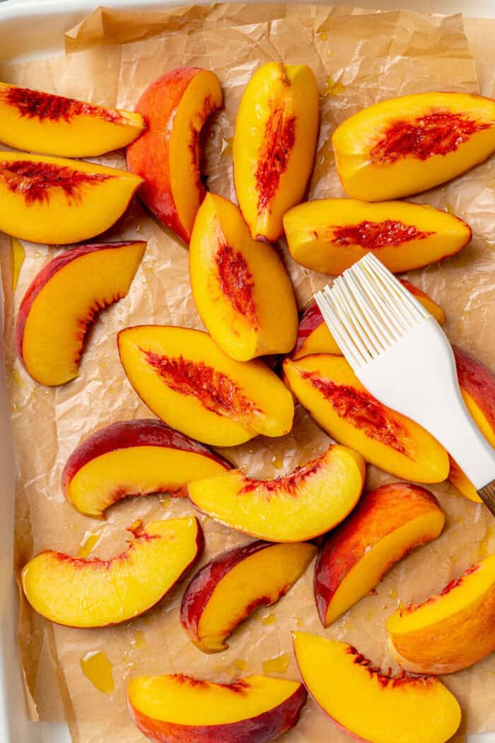 Oil is brushed onto fresh peach slices before grilling them.