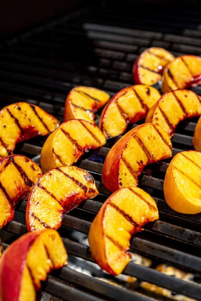 Peach slices cook on the grill with char marks visible.