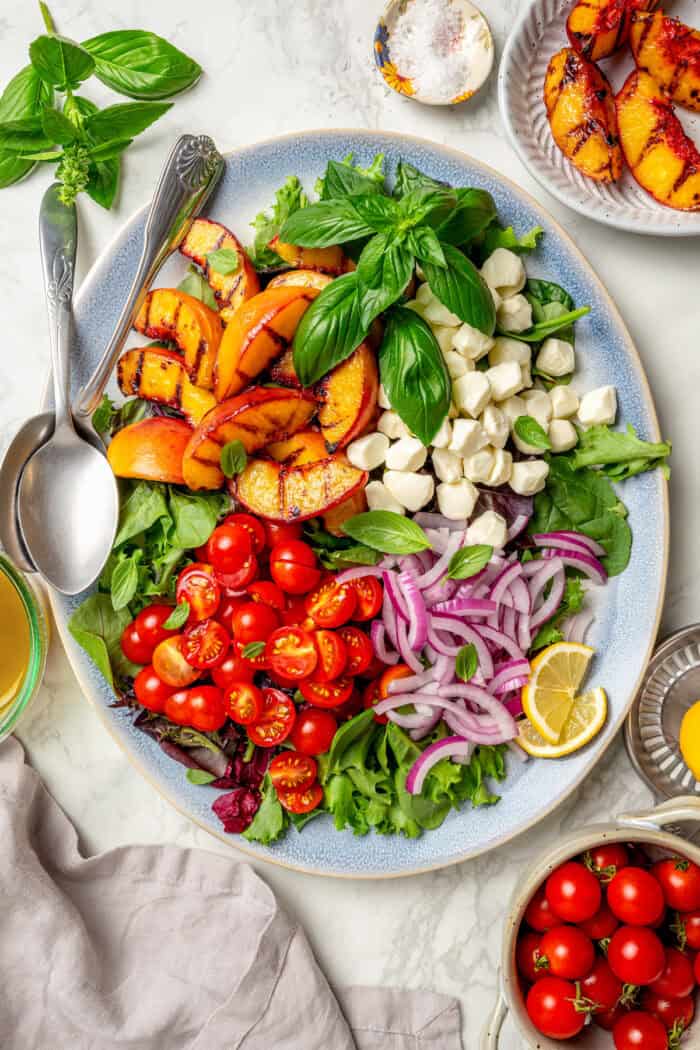 Salad greens are topped with grilled peach slices, red onion, fresh mozzarella, cherry tomatees, and basil leaves.