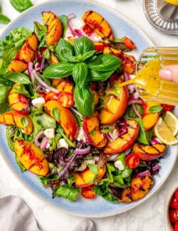 Dressing is poured over a serving platter of grilled peach salad.