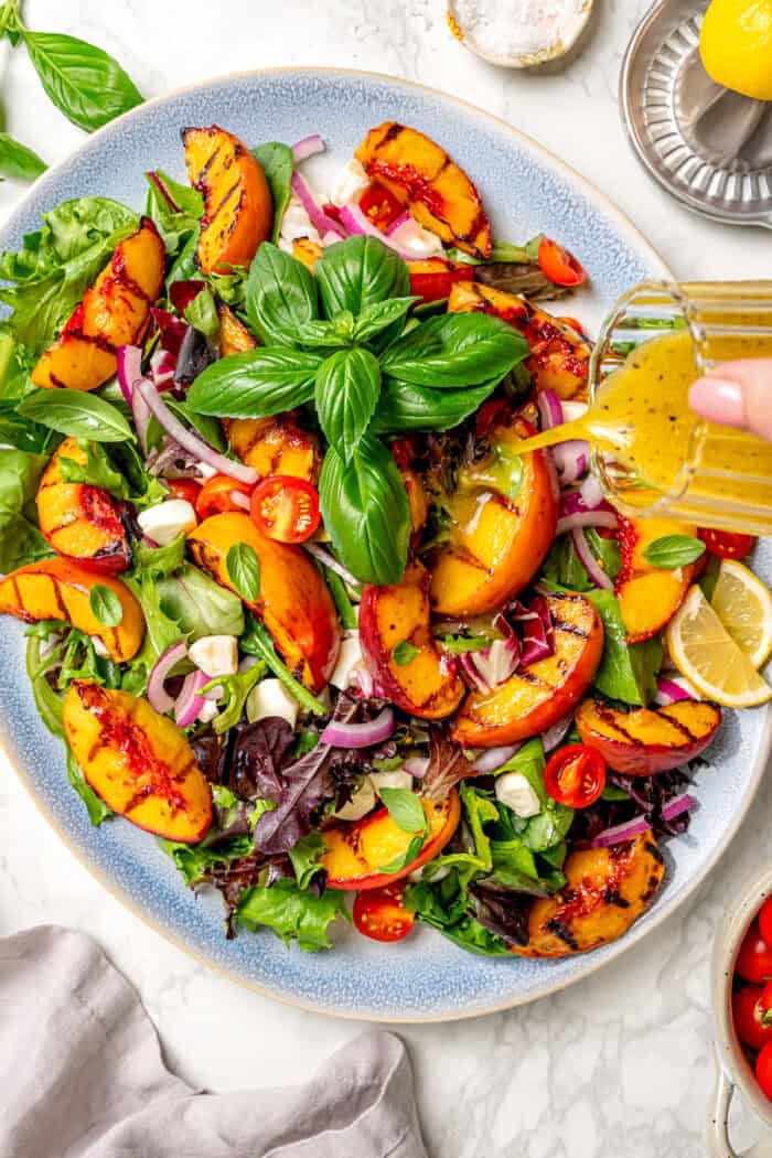 Dressing is poured over a serving platter of grilled peach salad.