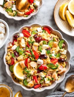 Bowls of lemon chicken orzo salad next to a serving bowl of salad.