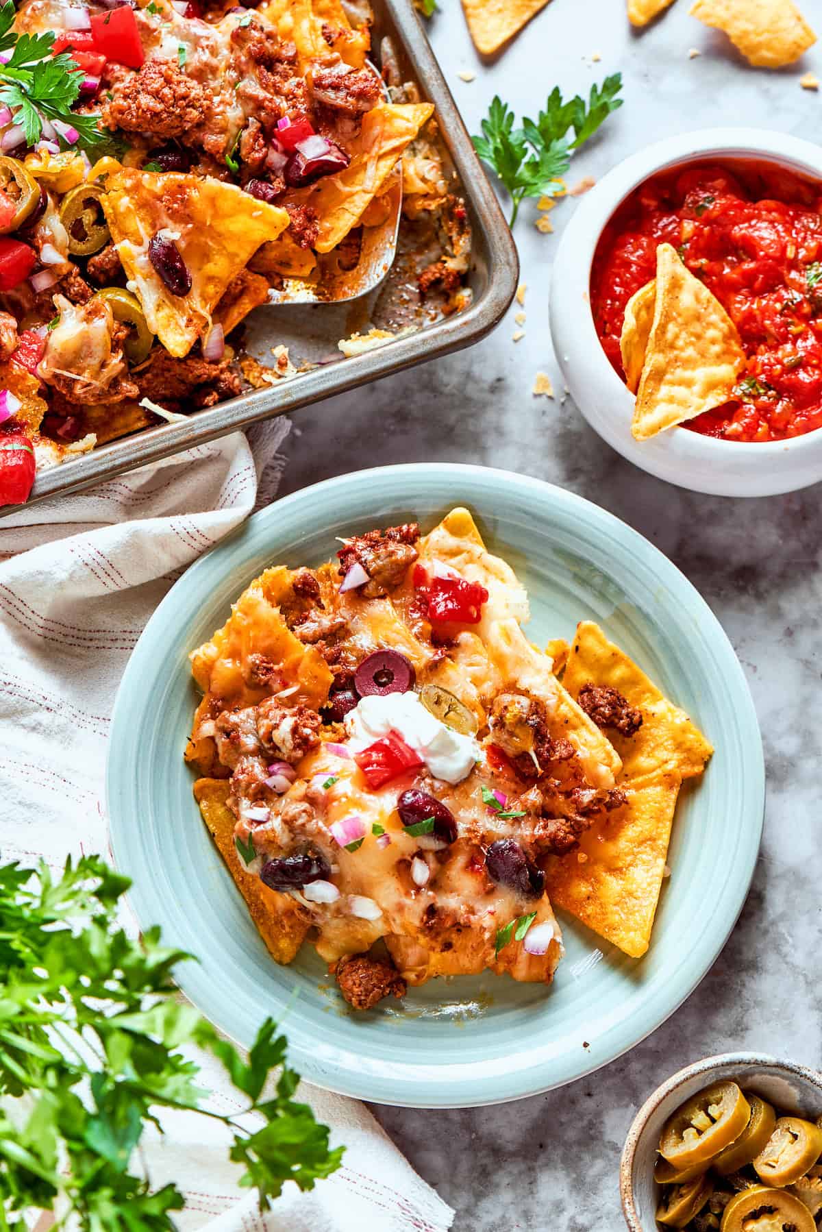A plate of macho nachos next to a tray of nachos and a bowl of salsa.