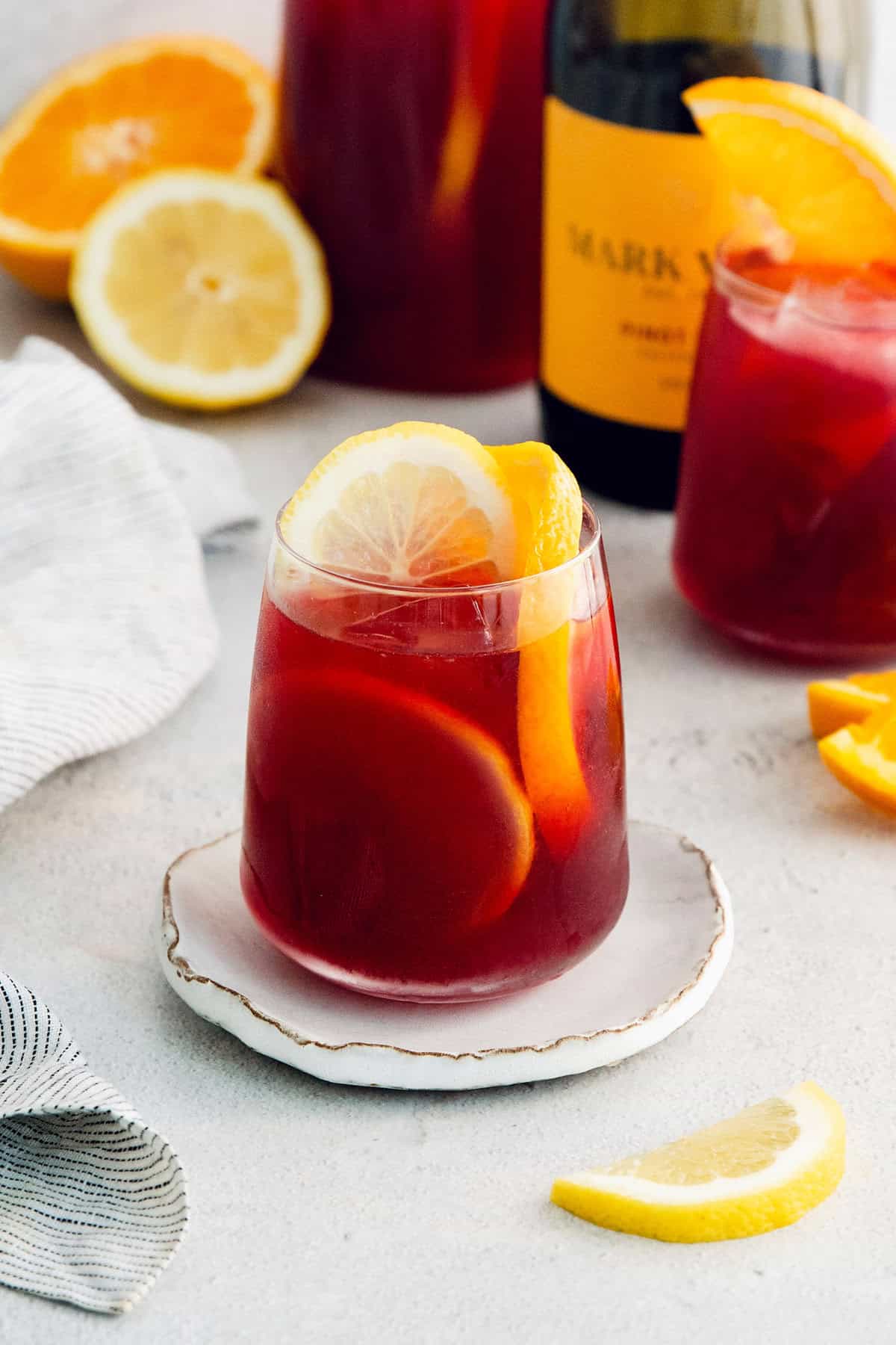 A glass of red tinto de verano is served on a white plate with more glasses behind it.