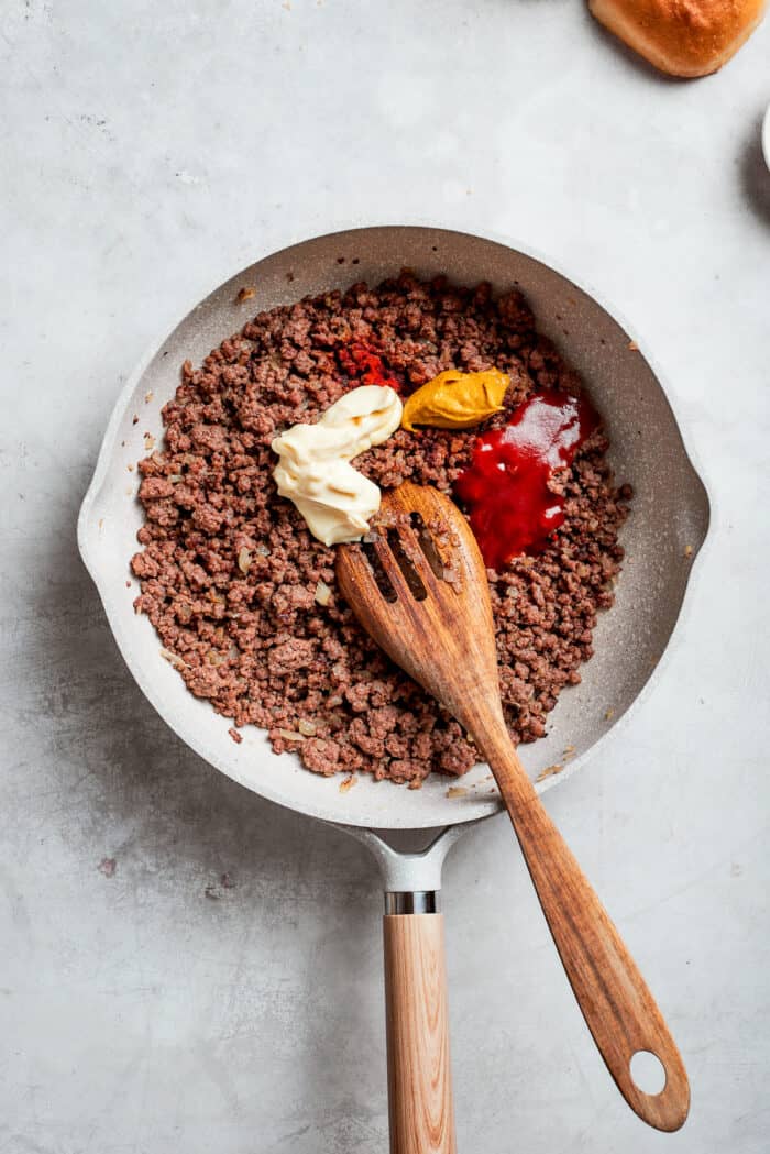 Condiments including mayonnaise, mustard, ketchup, and Worcestershire sauce are added to a pan of browned beef.