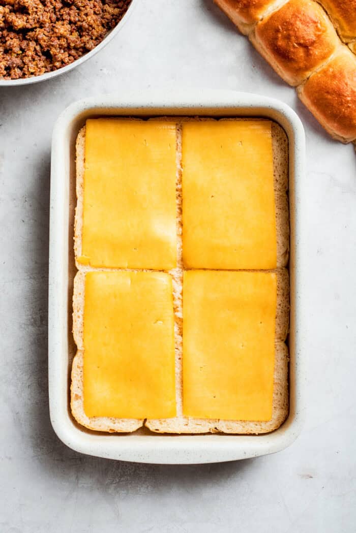 Sliced cheese is placed on top of sliced rolls.