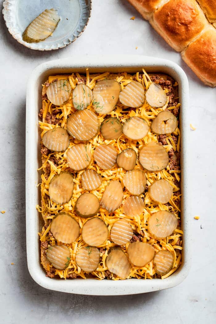 Sliced pickles are added to cheese on top of sliders.