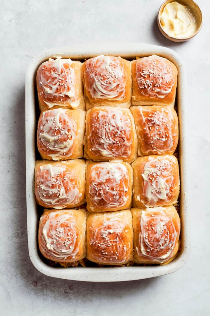 Melted butter is brushed on top of cheeseburger sliders rolls.