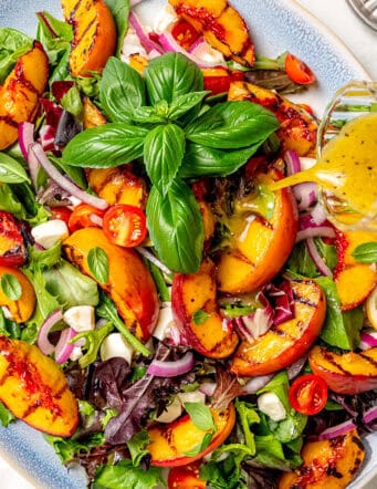 pouring dressing over a platter of grilled peach salad