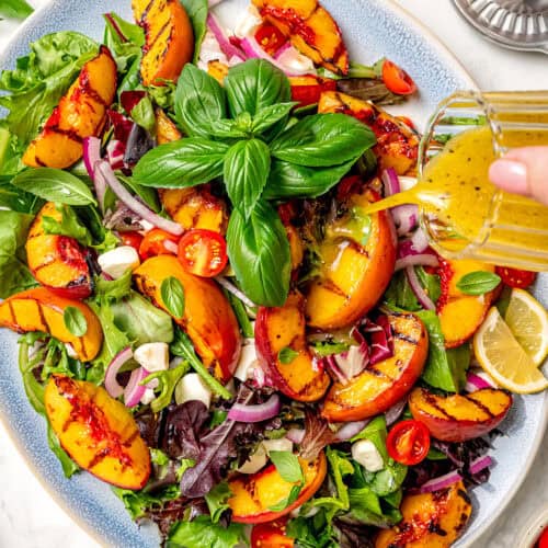 pouring dressing over a platter of grilled peach salad