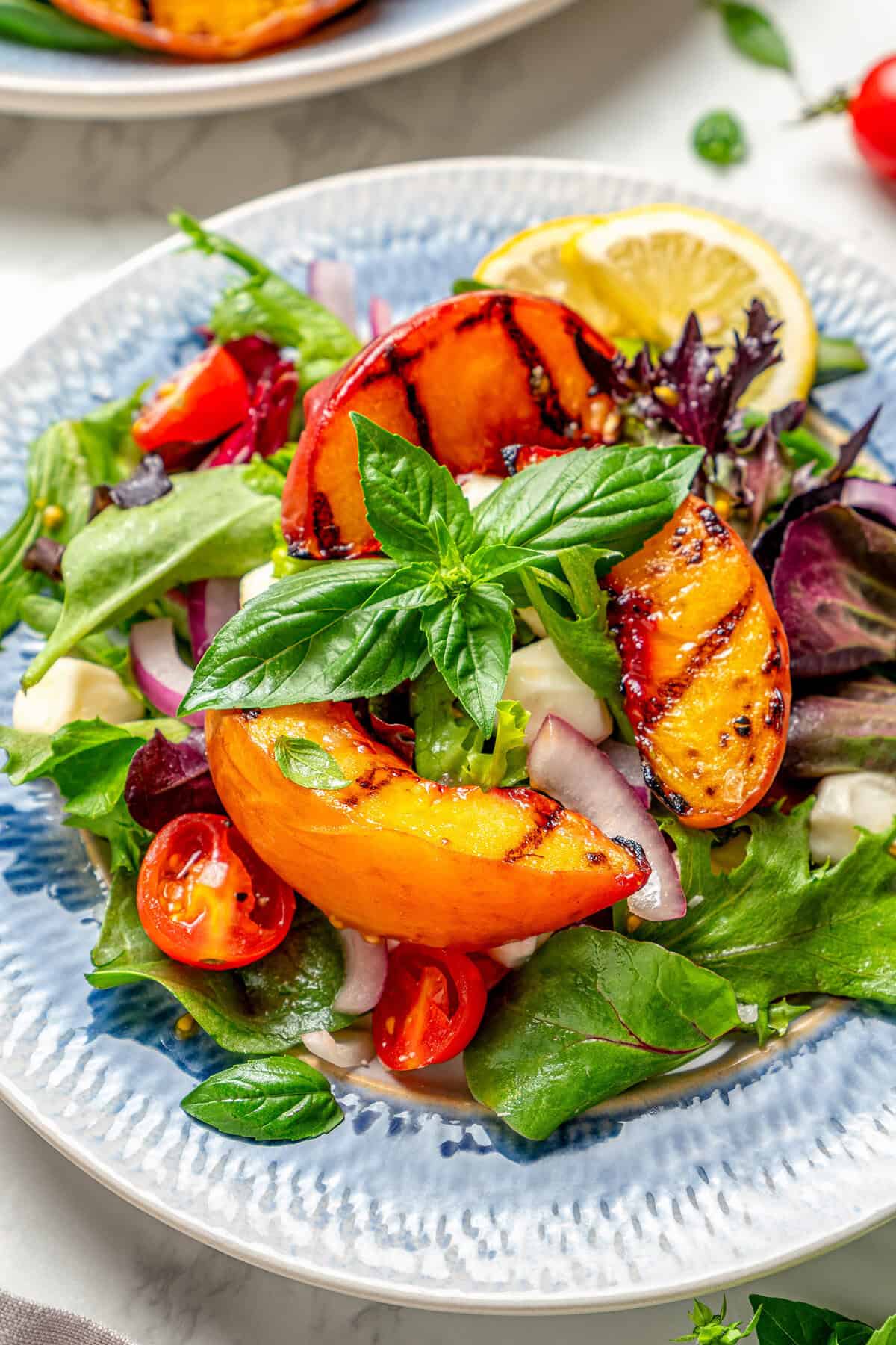 an individual plate of salad with grilled peaches and basil