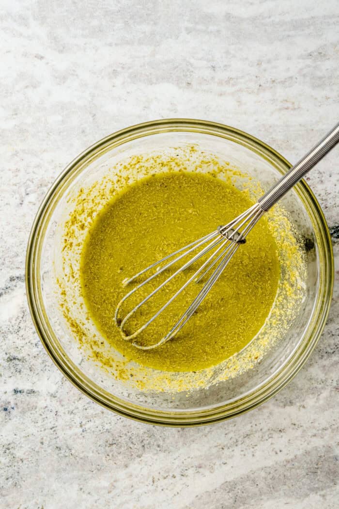 Ranch dressing and pesto sauce are whisked together in a bowl.