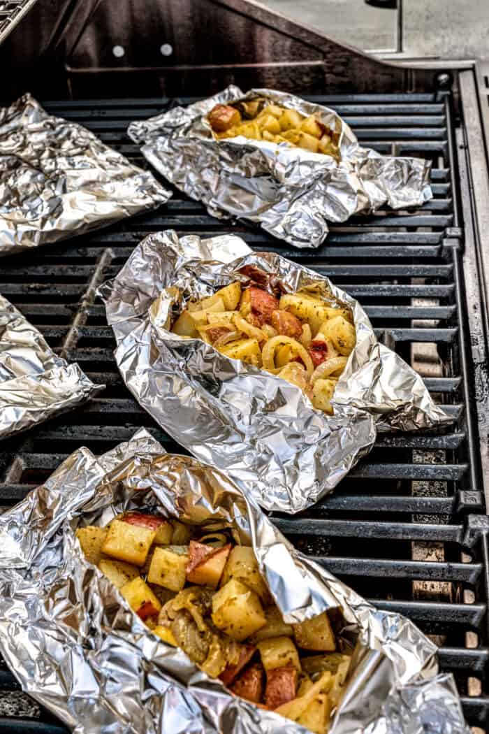 Potatoes wrapped in foil cook on the grill.