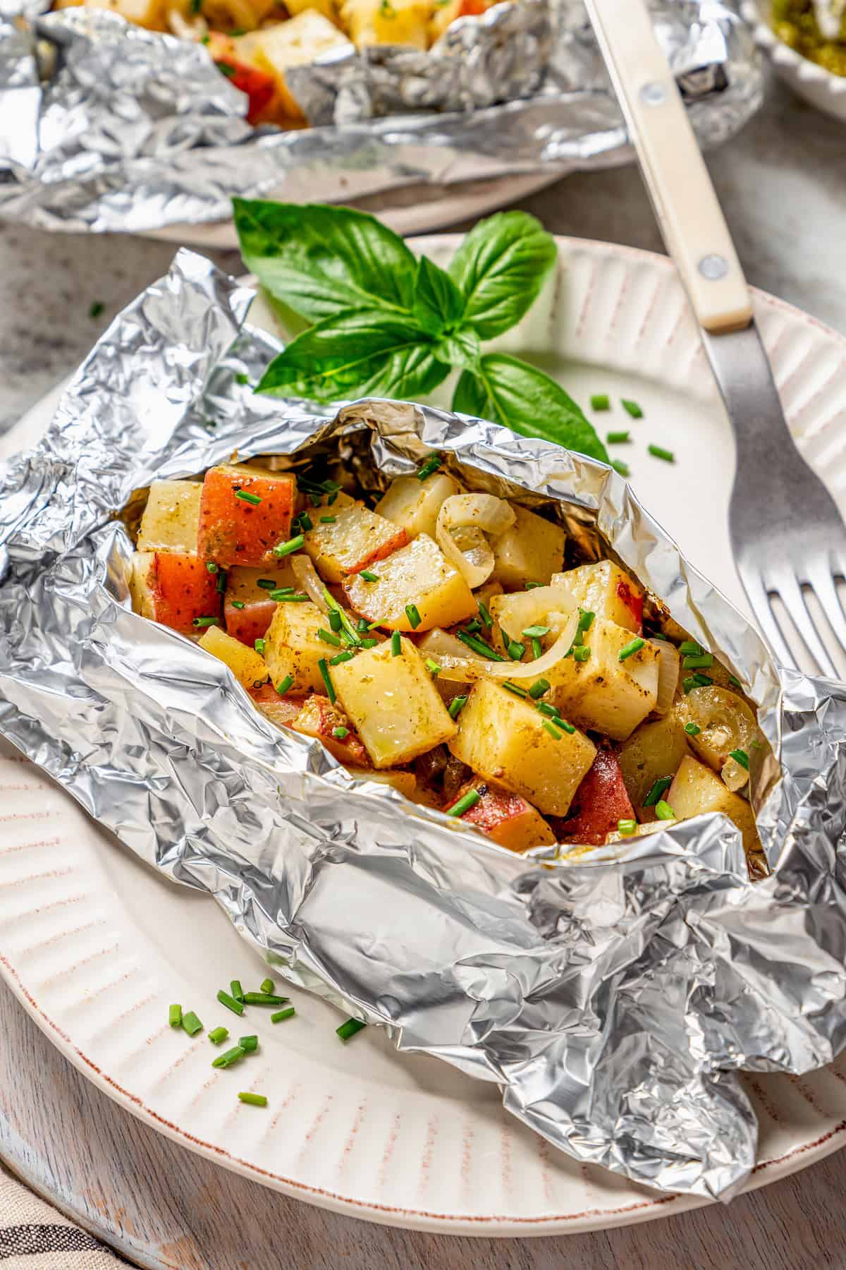 A grilled potato packet is opened to show the cooked potatoes inside.