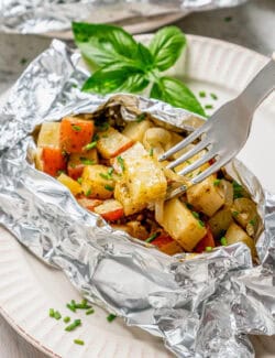 A fork picks up a piece of potato from a grilled potato packet.