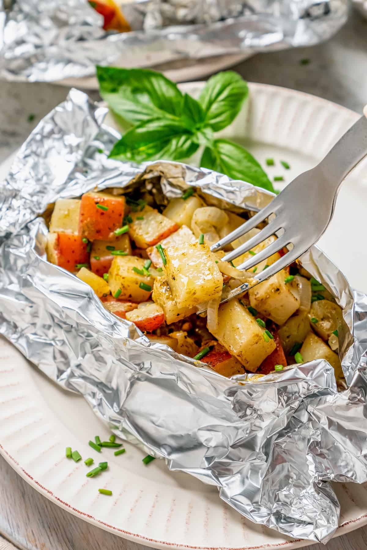 Savory Grilled Potato Packets feature grilled potatoes in foil dressed in tangy, garlicky pesto-ranch sauce and ready in less than 30 minutes. A fork picks up a piece of potato from a grilled potato packet.